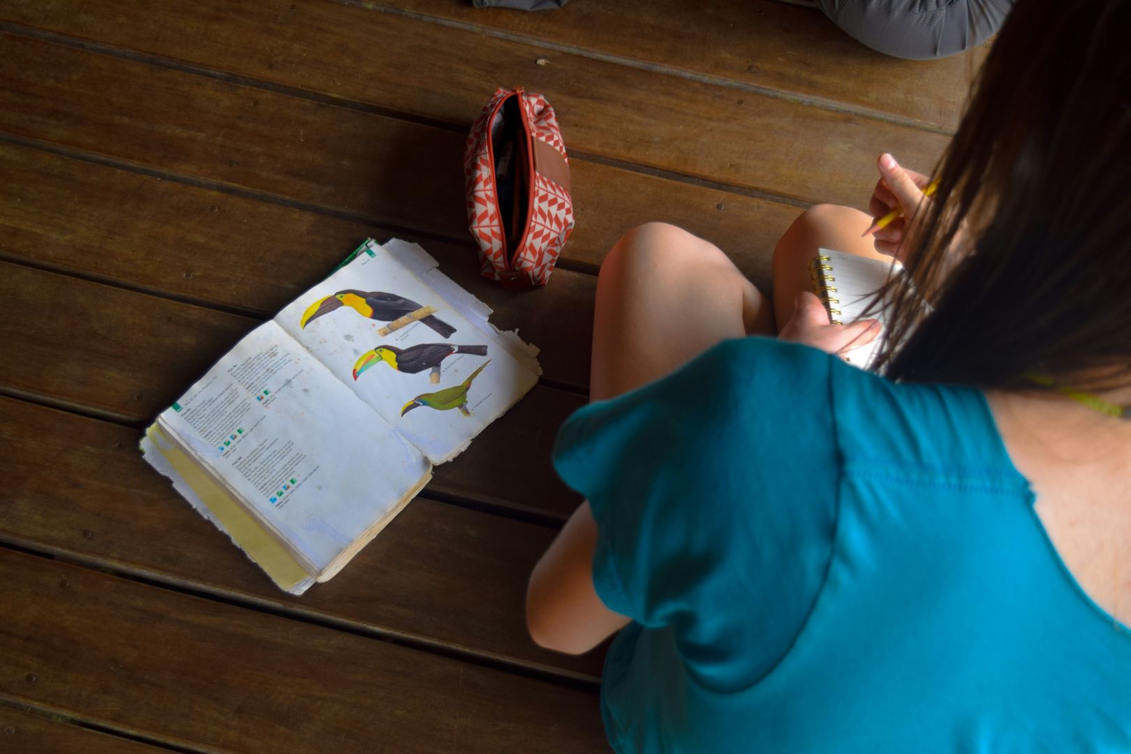 A person sitting on the floor with a book, notebook, and pencil